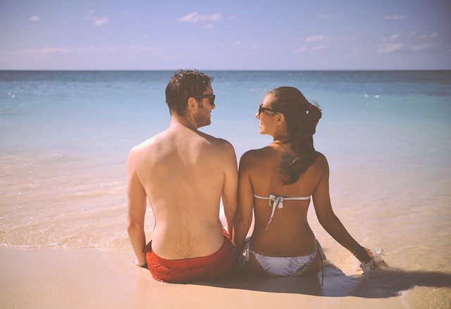 Muž a žena v plavkách sedia na pláži pri mori a pozerajú na seba.jpg