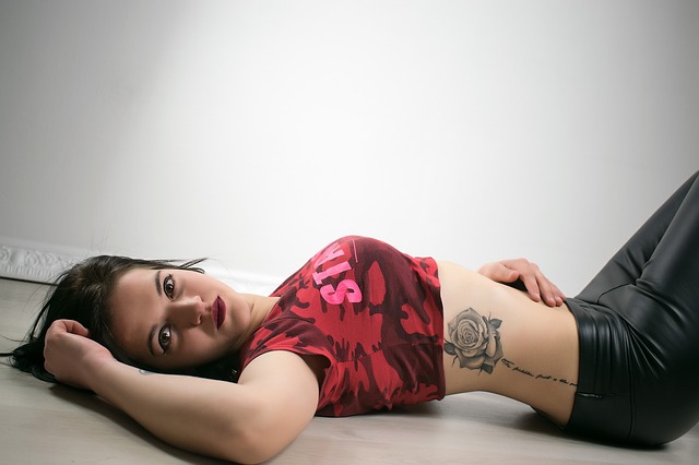 Žena v krátkom červenom tričku s tetovaním ruže na boku leží na podlahe.jpg