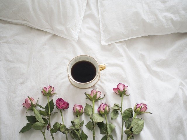 Posteľ, na ktorej je šálka s kávou a ružové ruže